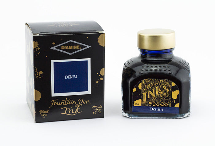 A glass bottle of 80ml Diamine Denim fountain pen ink next to its packaging box, in front of a white background.