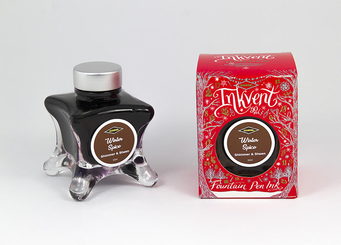 A glass bottle of 50ml Diamine Red Edition Inkvent Winter Spice Shimmer fountain pen ink next to packaging box, in front of a white background.