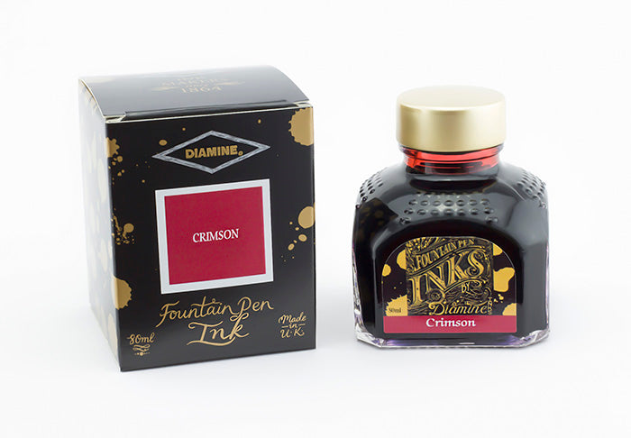 A glass bottle of 80ml Diamine Crimson fountain pen ink next to its packaging box, in front of a white background.