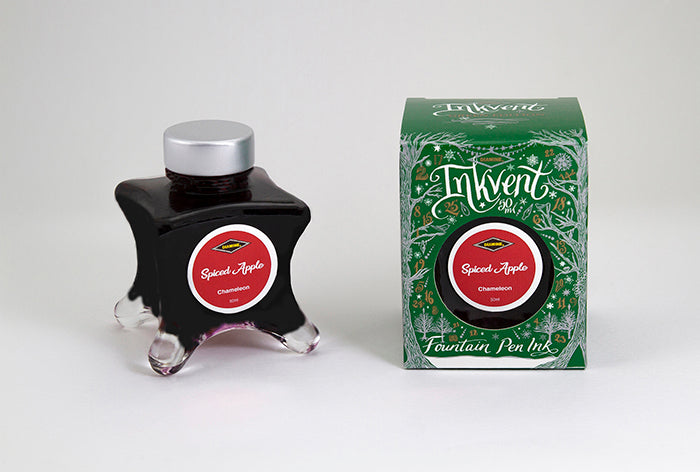 A glass bottle of 50ml Diamine Green Edition Inkvent Spiced Apple chameleon fountain pen ink next to packaging box, in front of a white background.