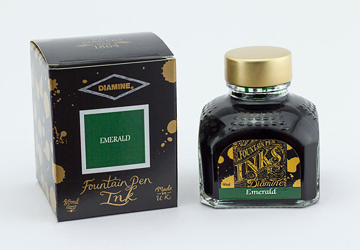 A glass bottle of 80ml Diamine Emerald fountain pen ink next to its packaging box, in front of a white background.