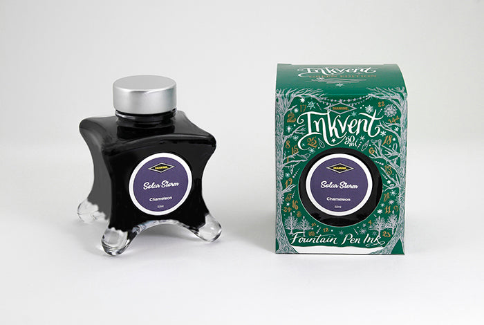 A glass bottle of 50ml Diamine Green Edition Inkvent Solar Storm chameleon fountain pen ink next to packaging box, in front of a white background.
