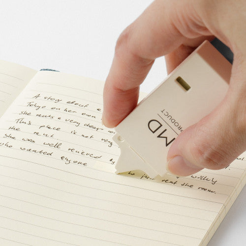 Hand demonstrating using MD Paper company product "writing correction tape" in cream colour on white background.