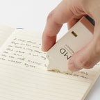Hand demonstrating using MD Paper company product "writing correction tape" in cream colour on white background.