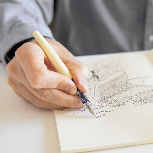 Hand using MD fountain pen to sketch out city scene.