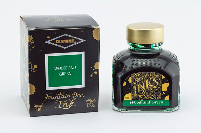 A glass bottle of 80ml Diamine Woodland Green fountain pen ink next to its packaging box, in front of a white background.