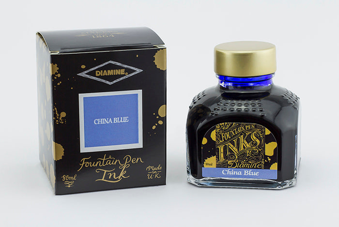 A glass bottle of 80ml Diamine China Blue fountain pen ink next to its packaging box, in front of a white background.