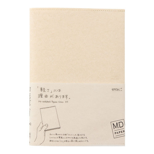 A beige notebook with a white paper band around the middle, featuring Japanese text and a simple illustration of a hand holding a notebook. The brand 'MD PAPER' is visible on the lower right of the band.
