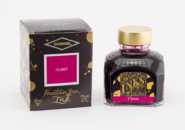 A glass bottle of 80ml Diamine Claret fountain pen ink next to its packaging box, in front of a white background.