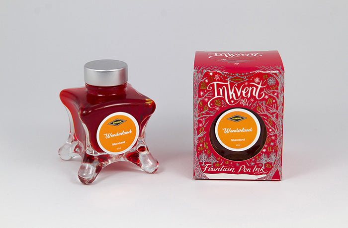 A glass bottle of 50ml Diamine Red Edition Inkvent Wonderland fountain pen ink next to packaging box, in front of a white background.