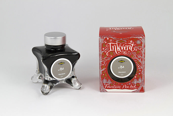 A glass bottle of 50ml Diamine Red Edition Inkvent Ash fountain pen ink next to packaging box, in front of a white background.