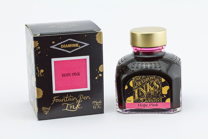 A glass bottle of 80ml Diamine Hope Pink fountain pen ink next to its packaging box, in front of a white background.