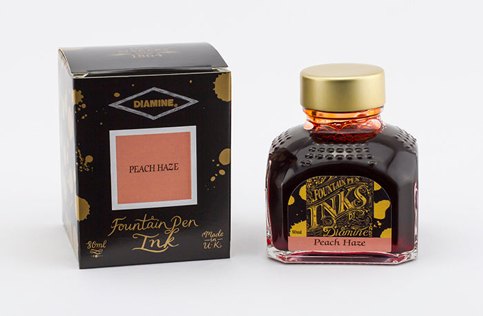 A glass bottle of 80ml Diamine Peach Haze fountain pen ink next to its packaging box, in front of a white background.