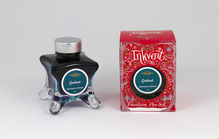 A glass bottle of 50ml Diamine Red Edition Inkvent Garland Shimmer & Sheen fountain pen ink next to packaging box, in front of a white background.