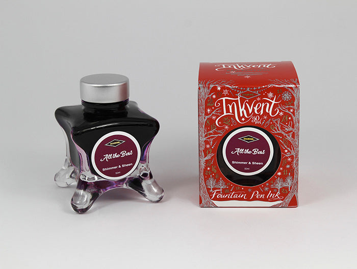 A glass bottle of 50ml Diamine Red Edition Inkvent All the Best Shimmer fountain pen ink next to packaging box, in front of a white background.