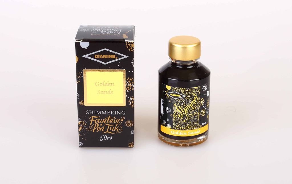 A glass bottle of 50ml Diamine Golden Sands shimmering fountain pen ink next to its packaging box, in front of a white background.