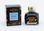 A glass bottle of 80ml Diamine Beau Blue fountain pen ink next to its packaging box, in front of a white background.