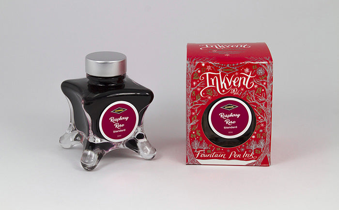 A glass bottle of 50ml Diamine Red Edition Inkvent Raspberry Rose fountain pen ink next to packaging box, in front of a white background.