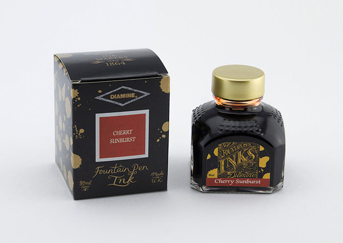 A glass bottle of 80ml Diamine Cherry Sunburst fountain pen ink next to its packaging box, in front of a white background.