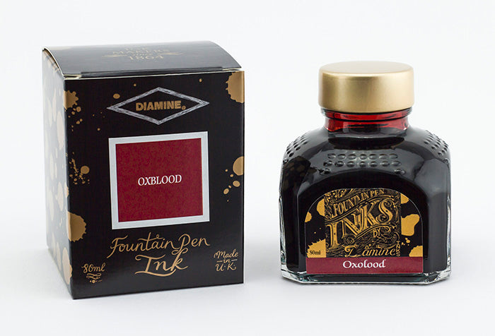 A glass bottle of 80ml Diamine Oxblood fountain pen ink next to its packaging box, in front of a white background.