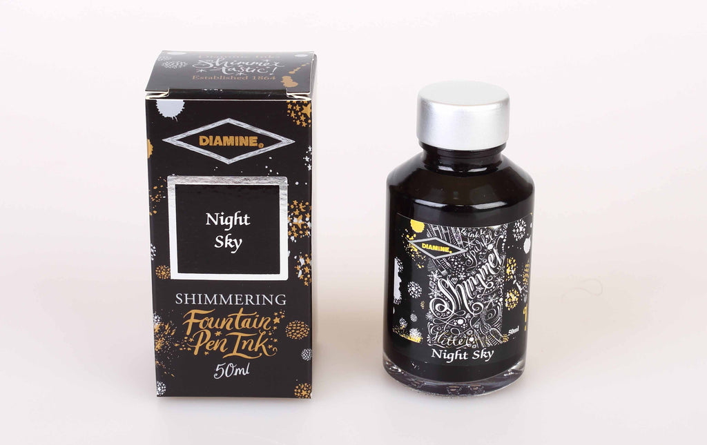 A glass bottle of 50ml Diamine Night Sky shimmering fountain pen ink next to its packaging box, in front of a white background.