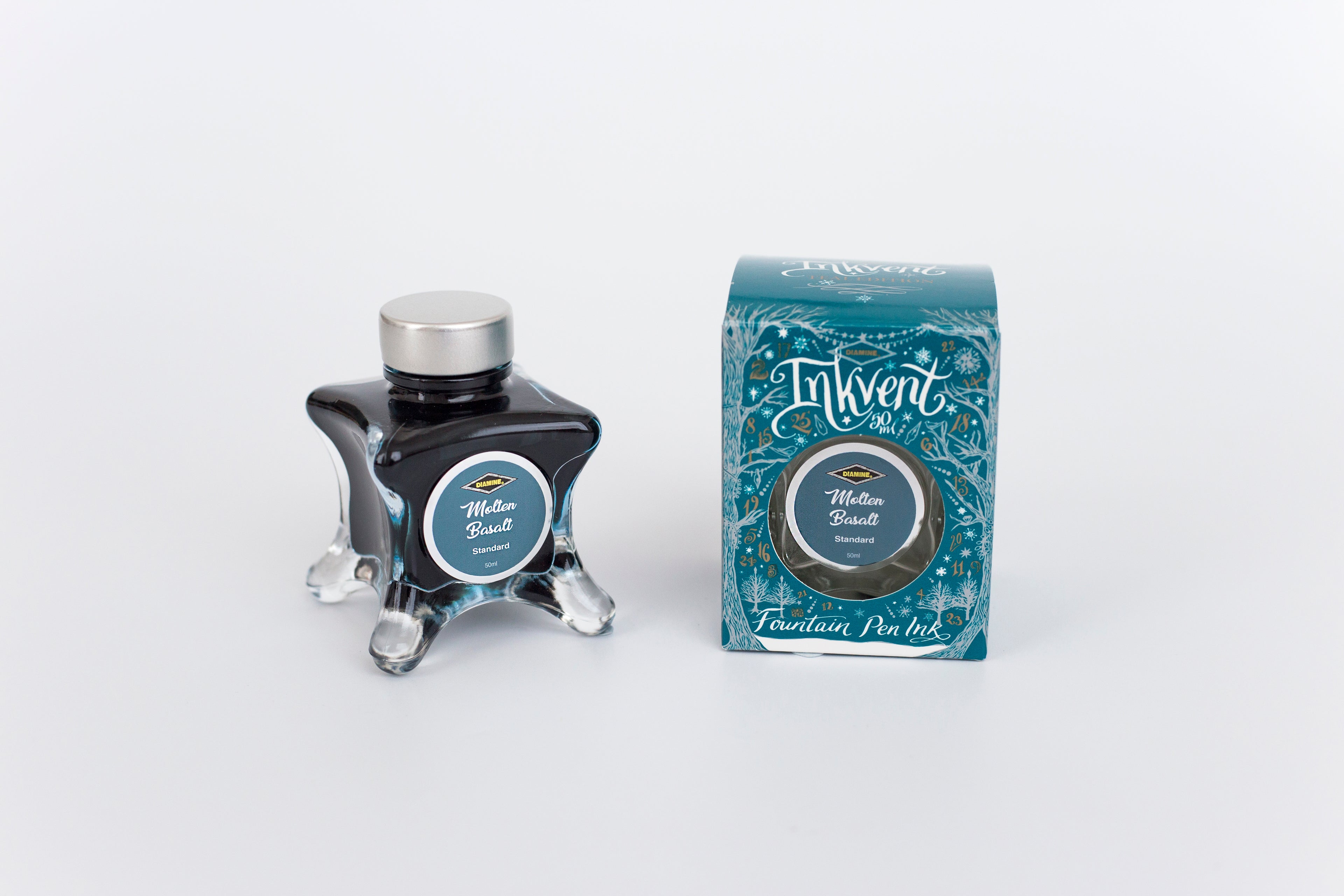 Glass bottle of 50ml Diamine Teal Edition Inkvent Molten Basalt fountain pen ink next to Teal coloured and Christmas-themed packaging box, in front of a white background.