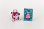 Glass bottle of 50ml Diamine Teal Edition Inkvent Mittens pigment fountain pen ink next to Teal coloured and Christmas-themed packaging box, in front of a white background.