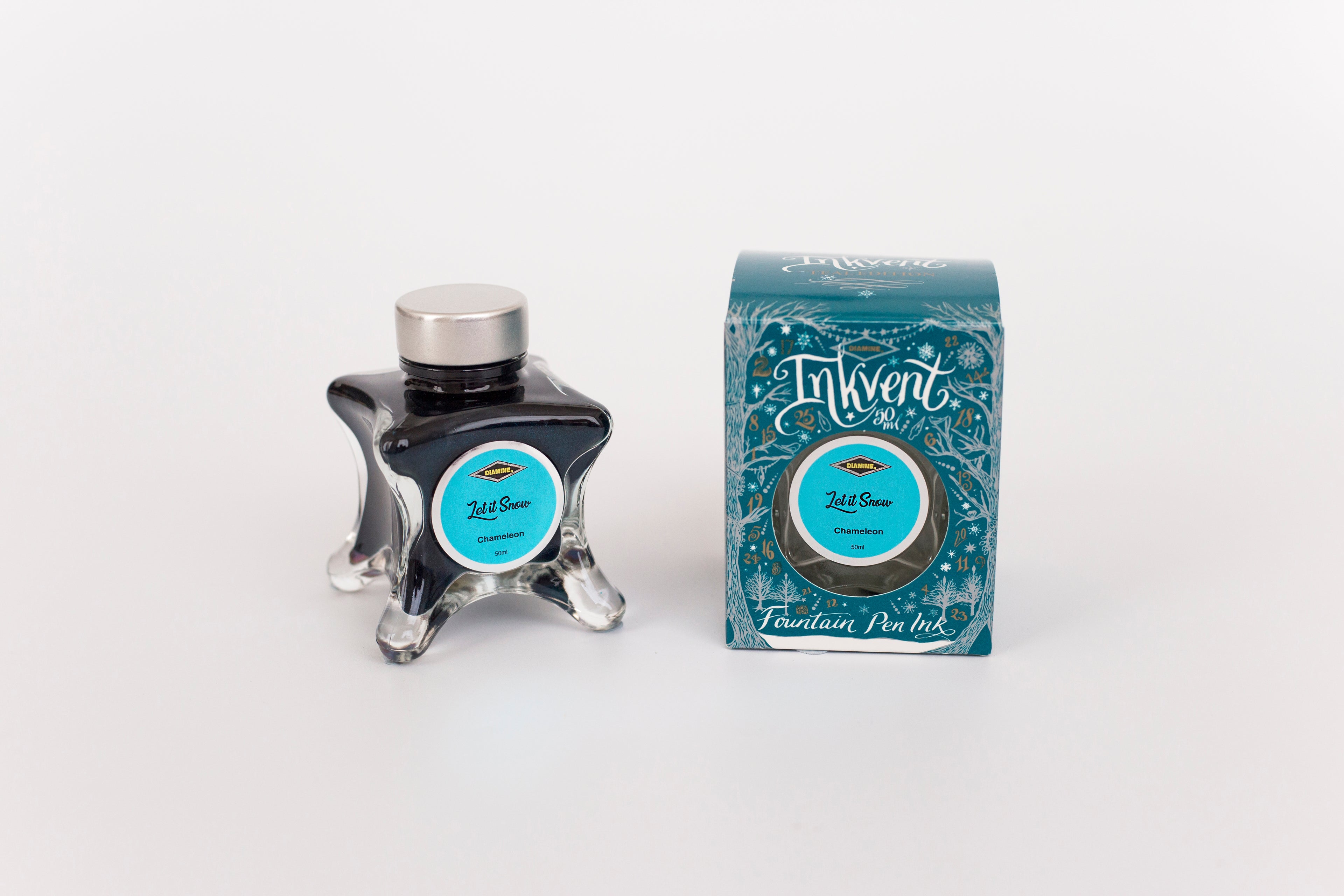 Glass bottle of 50ml Diamine Teal Edition Inkvent Let it Snow chameleon fountain pen ink next to Teal coloured and Christmas-themed packaging box, in front of a white background.