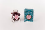 Glass bottle of 50ml Diamine Teal Edition Inkvent Blush fountain pen ink next to Teal coloured and Christmas-themed packaging box, in front of a white background.