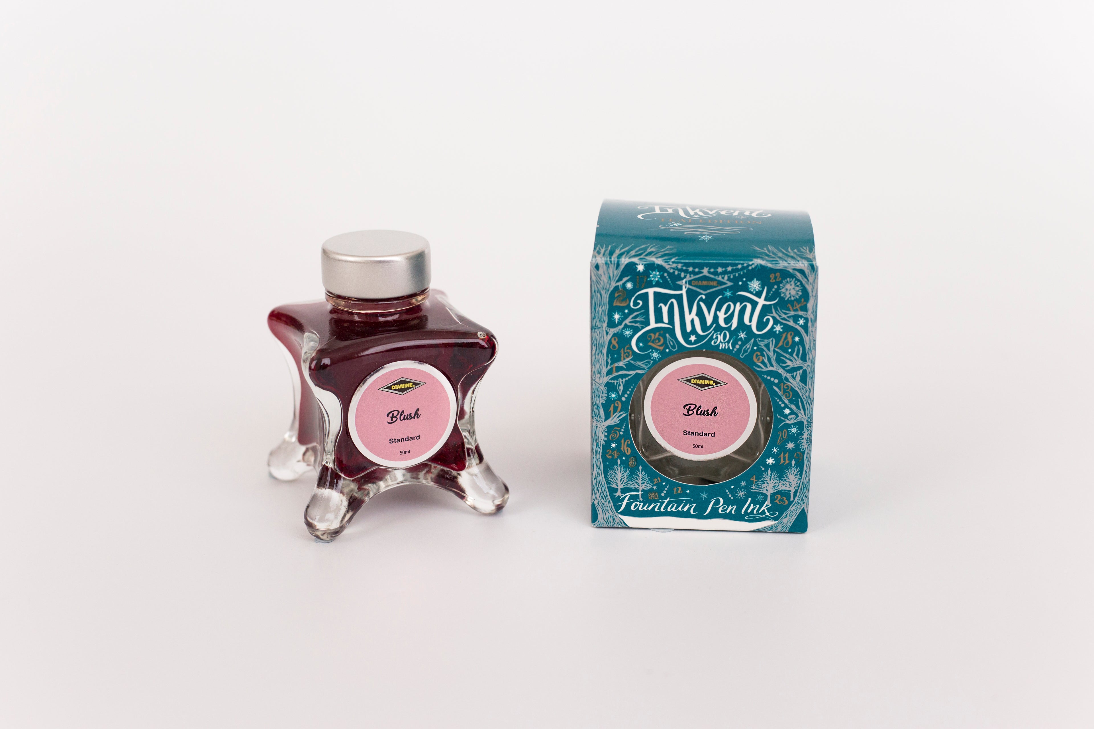 Glass bottle of 50ml Diamine Teal Edition Inkvent Blush fountain pen ink next to Teal coloured and Christmas-themed packaging box, in front of a white background.
