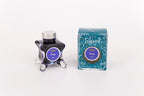 Glass bottle of 50ml Diamine Teal Edition Inkvent Energy sheen fountain pen ink next to Teal coloured and Christmas-themed packaging box, in front of a white background.