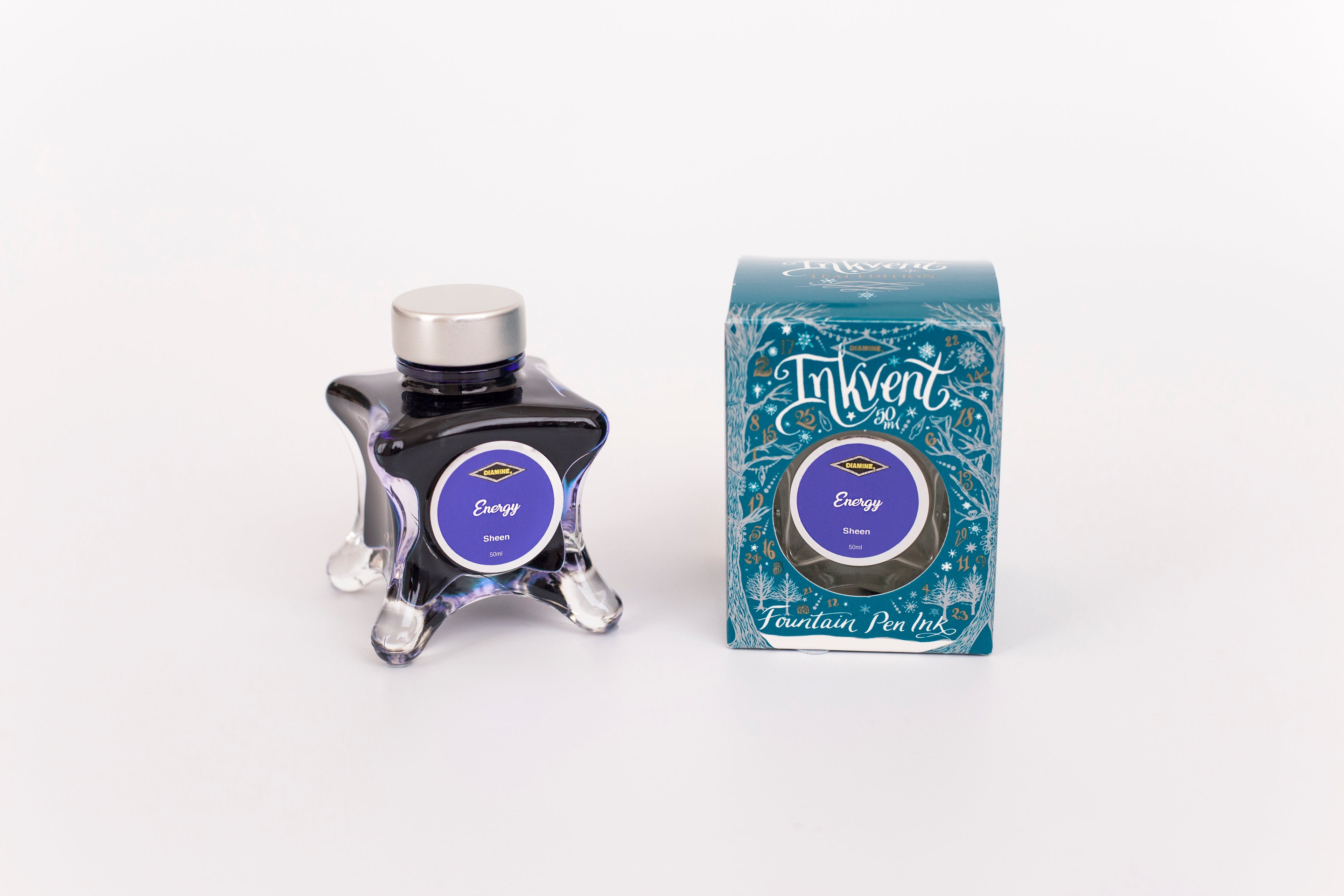 Glass bottle of 50ml Diamine Teal Edition Inkvent Energy sheen fountain pen ink next to Teal coloured and Christmas-themed packaging box, in front of a white background.