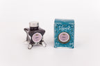 Glass bottle of 50ml Diamine Teal Edition Inkvent Antler pigment fountain pen ink next to Teal coloured and Christmas-themed packaging box, in front of a white background.