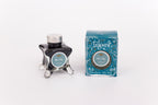 Glass bottle of 50ml Diamine Teal Edition Inkvent Fir & Fog fountain pen ink next to Teal coloured and Christmas-themed packaging box, in front of a white background.