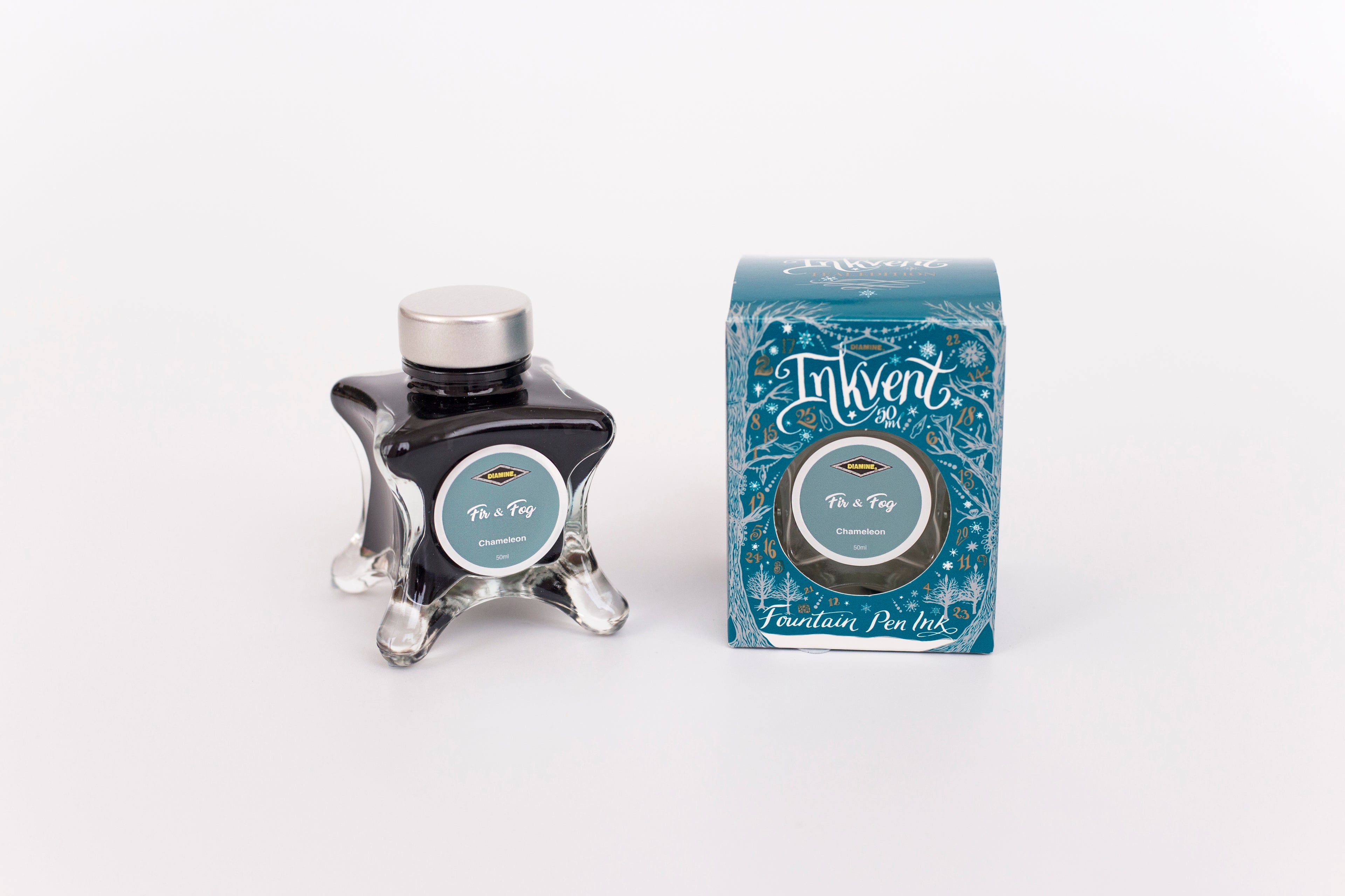 Glass bottle of 50ml Diamine Teal Edition Inkvent Fir & Fog fountain pen ink next to Teal coloured and Christmas-themed packaging box, in front of a white background.