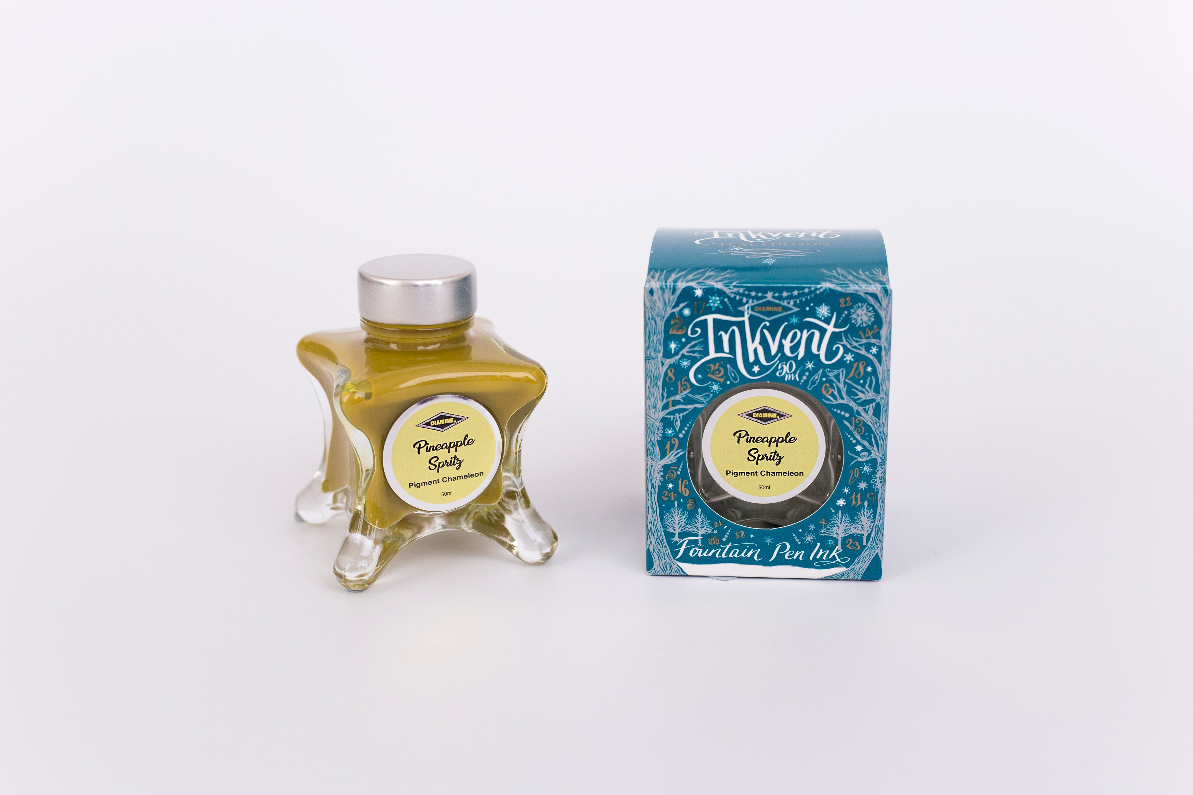 Glass bottle of 50ml Diamine Teal Edition Inkvent Pineapple Spritz pigment chameleon fountain pen ink next to Teal coloured and Christmas-themed packaging box, in front of a white background.