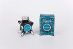 Glass bottle of 50ml Diamine Teal Edition Inkvent Celestial Skies fountain pen ink next to Teal coloured and Christmas-themed packaging box, in front of a white background.