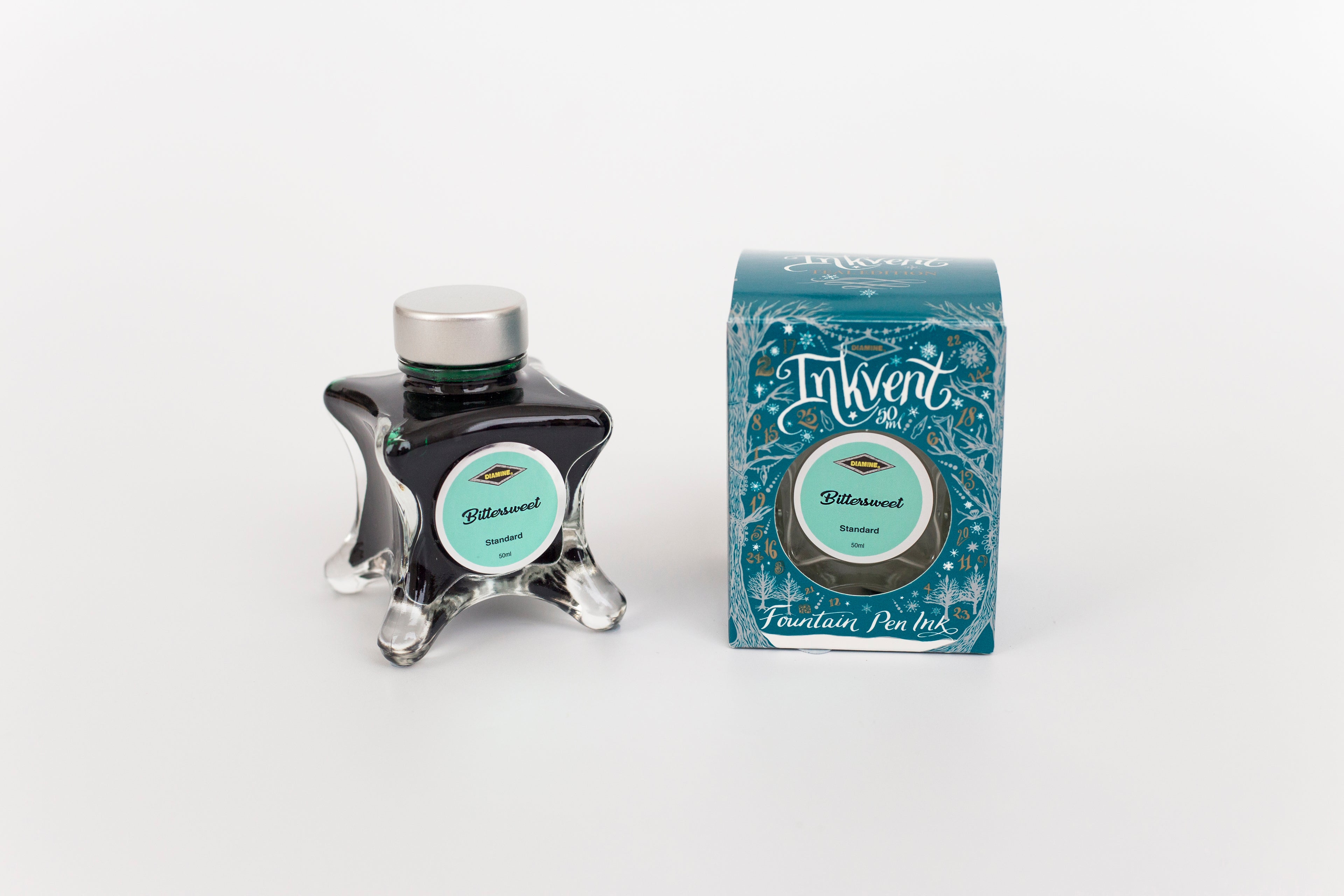 Glass bottle of 50ml Diamine Teal Edition Inkvent Bittersweet fountain pen ink next to Teal coloured and Christmas-themed packaging box, in front of a white background.