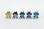 Group of five glass bottles of 50ml Diamine Teal Edition Inkvent pigment fountain pen ink, Pineapple Spritz, Smoky Tobacco, Myrrh the Merrier, Energy & BRRR!. Sitting in front of a white background.