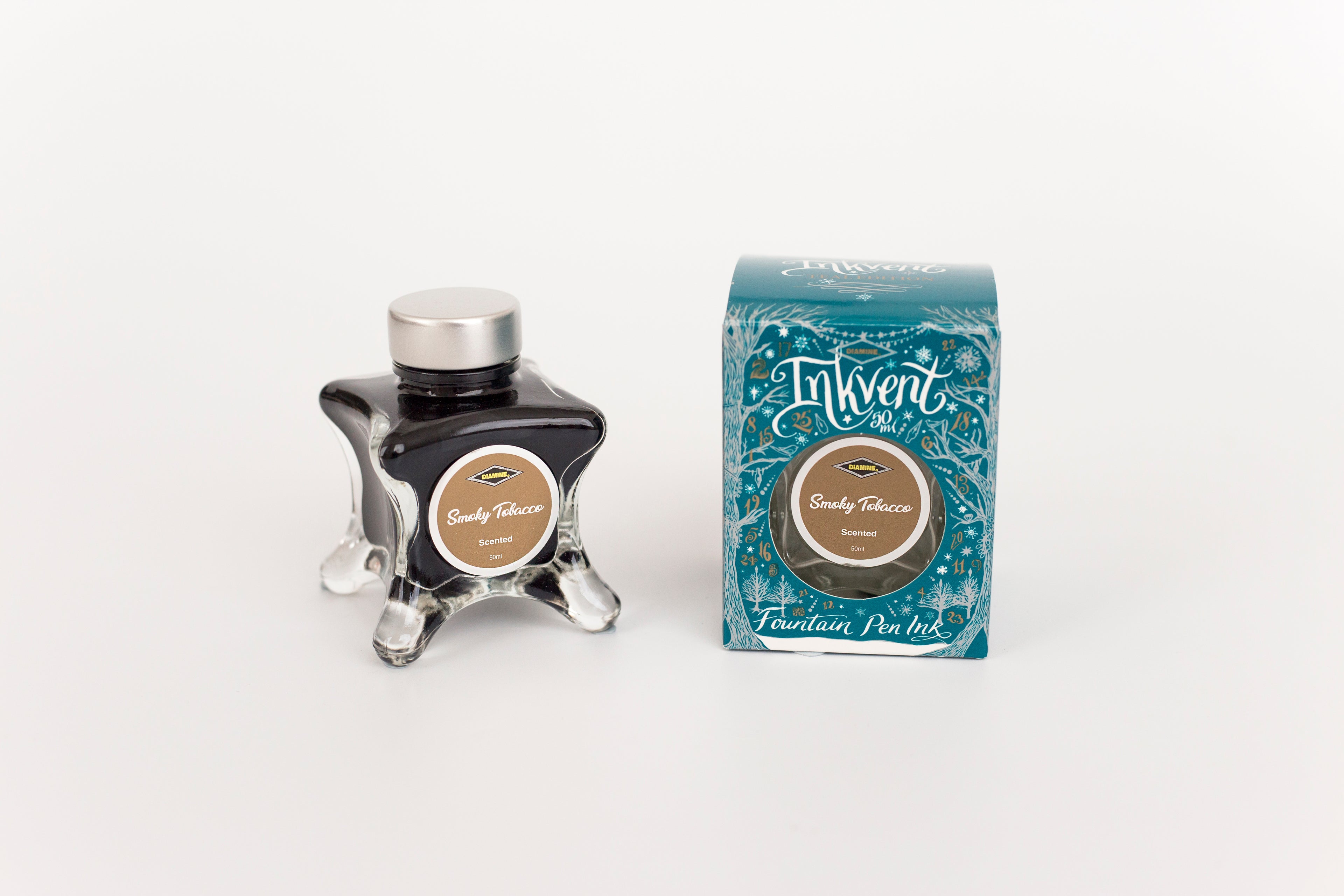Glass bottle of 50ml Diamine Teal Edition Inkvent Smoky Tobacco scented fountain pen ink next to Teal coloured and Christmas-themed packaging box, in front of a white background.