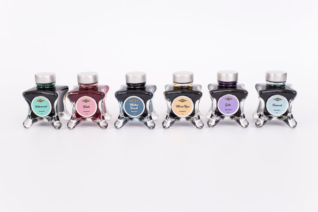 Group of six glass bottles of 50ml Diamine Teal Edition Inkvent pigment fountain pen ink, Bittersweet, Blush, Molten Basalt, Marie Rose, Gala & Overcast. Sitting in front of a white background.