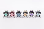 Group of six glass bottles of 50ml Diamine Teal Edition Inkvent pigment fountain pen ink, Bittersweet, Blush, Molten Basalt, Marie Rose, Gala & Overcast. Sitting in front of a white background.