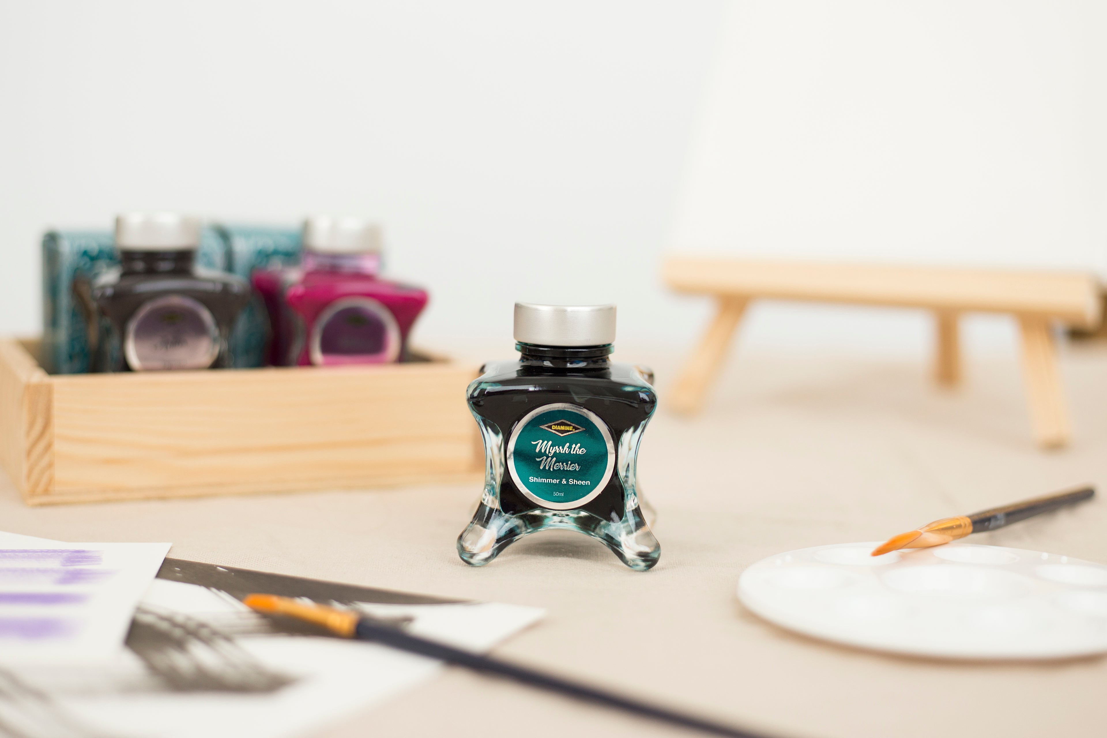 Diamine Myrrh the Merrier Fountain Pen Ink bottle with a brush and paper on a table.