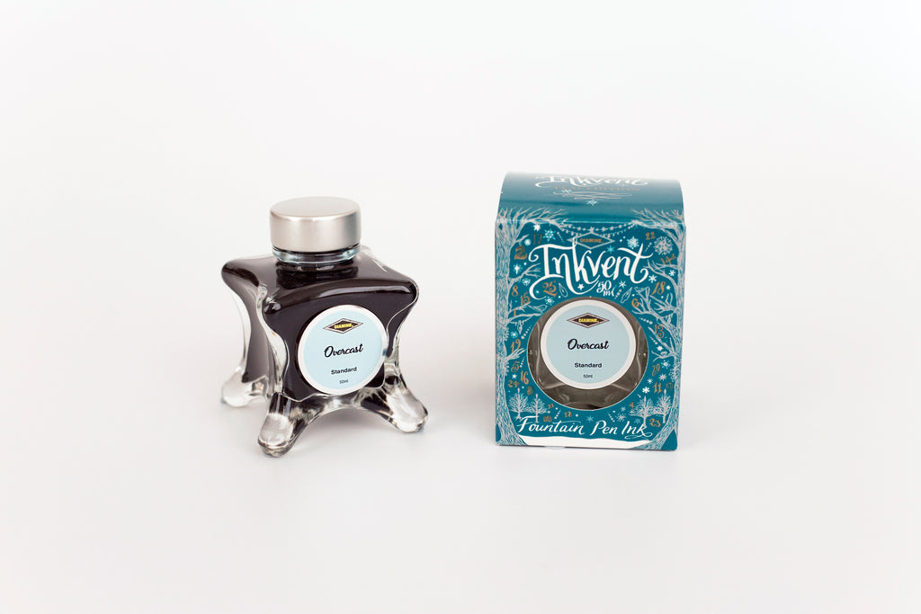 Glass bottle of 50ml Diamine Teal Edition Inkvent Overcast fountain pen ink next to Teal coloured and Christmas-themed packaging box, in front of a white background.