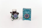 Glass bottle of 50ml Diamine Teal Edition Inkvent Dream Catcher extreme sheen fountain pen ink next to Teal coloured and Christmas-themed packaging box, in front of a white background.