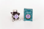 Glass bottle of 50ml Diamine Teal Edition Inkvent Gala fountain pen ink next to Teal coloured and Christmas-themed packaging box, in front of a white background.