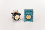 Glass bottle of 50ml Diamine Teal Edition Inkvent Marie Rose fountain pen ink next to Teal coloured and Christmas-themed packaging box, in front of a white background.