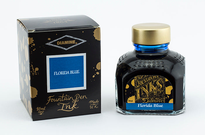 A glass bottle of 80ml Diamine Florida Blue fountain pen ink next to its packaging box, in front of a white background.