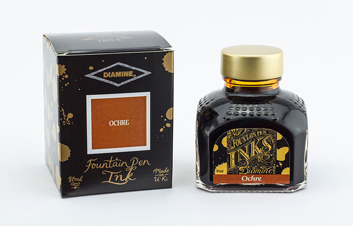 A glass bottle of 80ml Diamine Ochre fountain pen ink next to its packaging box, in front of a white background.