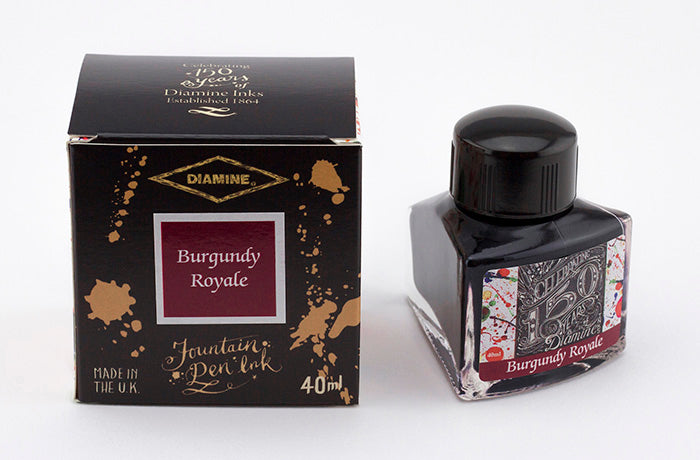 A glass bottle of 40ml Diamine 150th Anniversary Burgundy Royale fountain pen ink next to packaging box, in front of a white background.